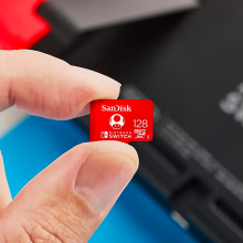 close-up of a person holding a sandisk microsd card in front of a standard nintendo switch console