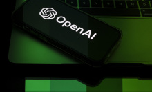 A phone displays the OpenAI logo bathed in green light. 