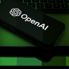 A phone displays the OpenAI logo bathed in green light. 