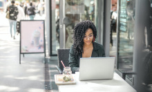 a woman sits outside a cafe working on her laptop