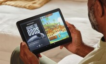 a person holds an Amazon fire HD 10 tablet while sitting on a cream colored couch