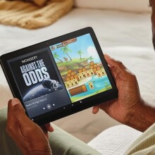 a person holds an Amazon fire HD 10 tablet while sitting on a cream colored couch