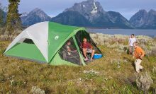 a family camps in a coleman tent in a grassy field