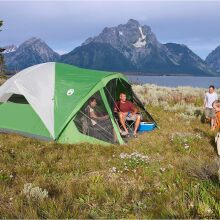 a family camps in a coleman tent in a grassy field