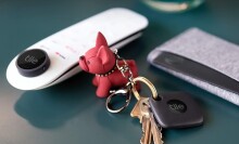 a side table includes a remote control, keys with a red dog keychain, and a wallet. All items have a tile bluetooth tracker attached.