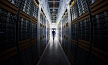 A man in silhouette, walking through racks of computers in a data center.