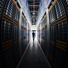 A man in silhouette, walking through racks of computers in a data center.