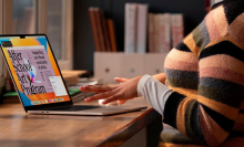 a close-up of a woman in striped sweater typing on a 15-inch m2 apple macbook air at a wooden table