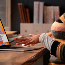 a close-up of a woman in striped sweater typing on a 15-inch m2 apple macbook air at a wooden table