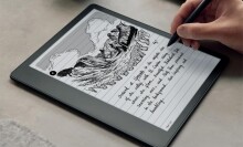 a right hand uses a digital pen on a kindle scribe with cursive handwriting on the screen and a drawing on a mountainous valley