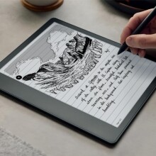 a right hand uses a digital pen on a kindle scribe with cursive handwriting on the screen and a drawing on a mountainous valley