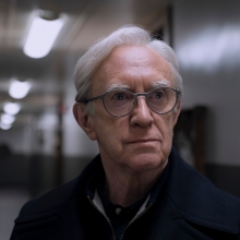 A man in glasses stands in a ship passage looking concerned.