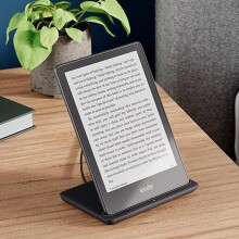 the kindle paperwhite signature edition sits on a wireless charger on a nightstand.