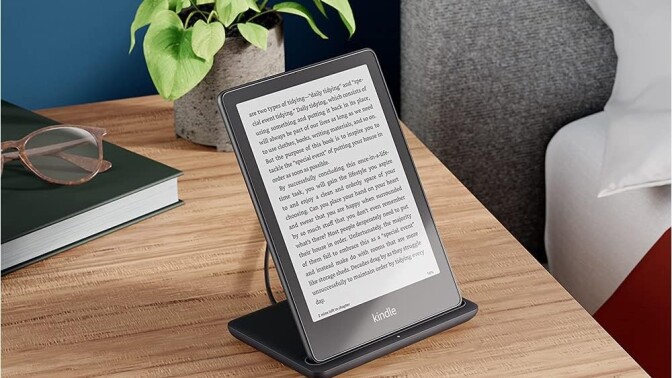 the kindle paperwhite signature edition sits on a wireless charger on a nightstand.