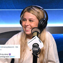 A woman sits in a studio wearing headphones and grinning.