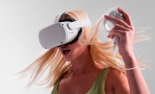 a person with long, blonde hair wears the meta quest 2 headset while using one of the hand tracking devices in her left hand