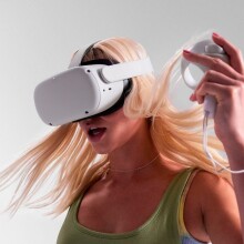 a person with long, blonde hair wears the meta quest 2 headset while using one of the hand tracking devices in her left hand