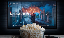 A TV screen is paused on the Netflix show "Bridgerton" with a bowl of popcorn sitting in front of it.