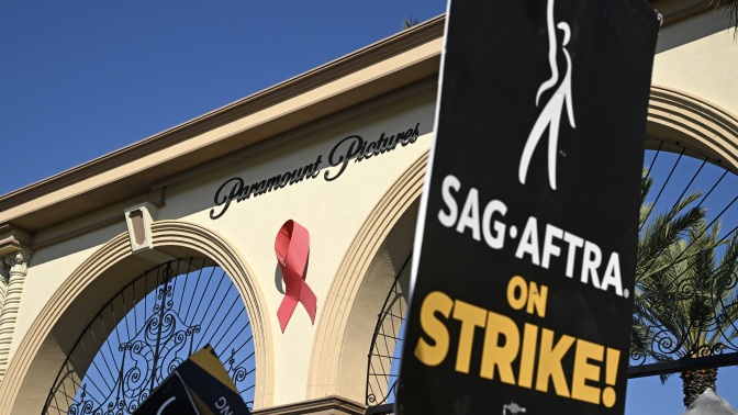 A black poster reading "SAG-AFTRA on strike!" outside the Paramount Pictures gate in Hollywood.