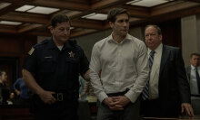 A man in a courtroom is led by a police officer.