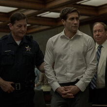 A man in a courtroom is led by a police officer.