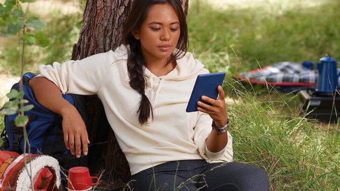 A girl sits outside and reads on her Amazon Kindle 