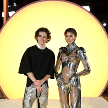 Timothee Chalamet and Zendaya on the 'Dune: Part 2' red carpet illuminated by a glowing yellow circle behind them.