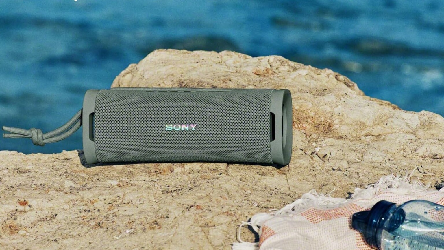 a portable sony bluetooth speaker sits on a towel atop a rock at the beach