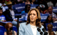 Vice President Kamala Harris looking serious in a pale blue suit at a campaign rally.