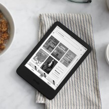 a kindle e-reader sits in a kitchen table next to a bowl of cereal