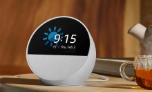 the amazon echo spot shows the time while sitting on a table with a cup of tea beside it