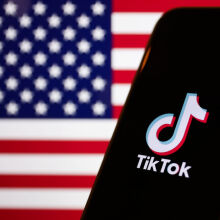 American flag displayed on a laptop screen and TikTok logo displayed on a phone screen.