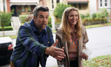 A man and a woman stand on the doorstep of a suburban road, looking excited.