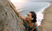 Women wearing Bose QuietComfort earbuds climbs a rock