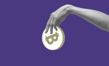 Hand holding abstract bitcoin against purple background.
