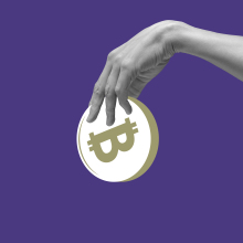 Hand holding abstract bitcoin against purple background.