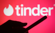 A red backdrop including the Tinder logo with the silhouette of a person's hand holding a phone. 