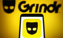 Grindr logo is seen on a smartphone and a backdrop