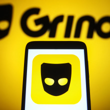 Grindr logo is seen on a smartphone and a backdrop