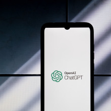 A phone displaying the ChatGPT logo against a shadowed backdrop.