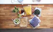 An assortment of stasher bags filled with soups, smoothies, and more on a kitchen counter.