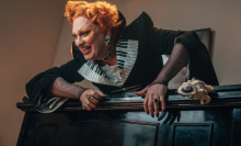 Jinkx Monsoon dressed as the Maestro atop a piano