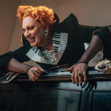 Jinkx Monsoon dressed as the Maestro atop a piano