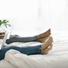 A couple lies on top of a bed, both with laptops on their laps.