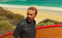 Nicolas Cage wears a wetsuit and holds a surfboard in a still from "The Surfer."