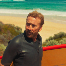 Nicolas Cage wears a wetsuit and holds a surfboard in a still from "The Surfer."