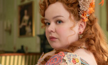 A woman in regency-era dress sits in a lavish room, a book in her hands.