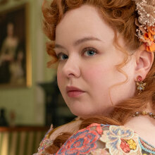 A woman in regency-era dress sits in a lavish room, a book in her hands.