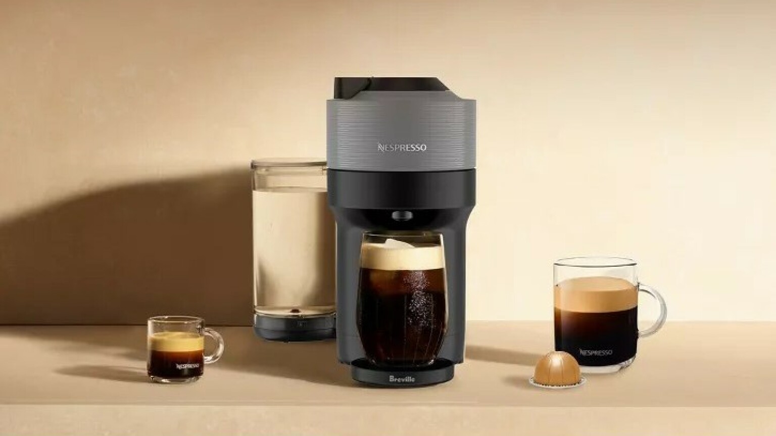 the nespresso vertuo pop+ machine sits on a counter with several coffee cups around the machine and one nespresso vertuo pod