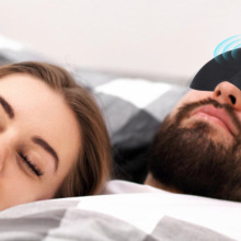 Person wearing black sleeping mask sleeping next to smiling person with eyes closed